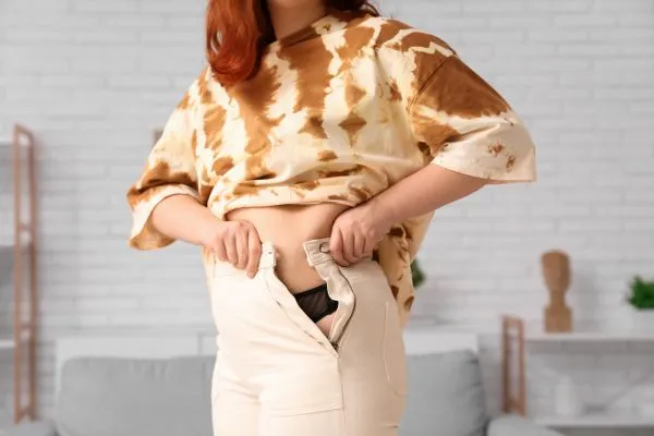 Image of woman trying to do her trousers up after pregnancy weight gain Bushey