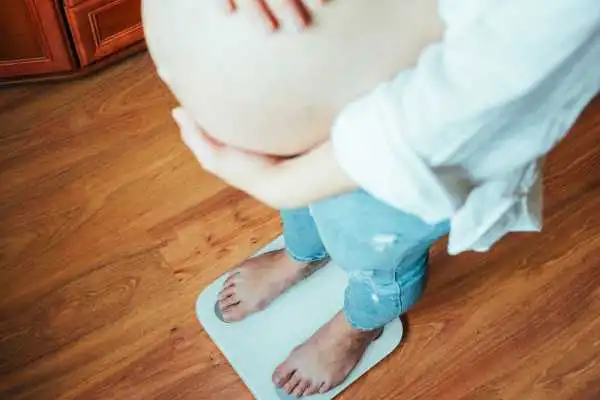 Image of woman weighing herself and experiencing weight gain through pregnancy Bushey